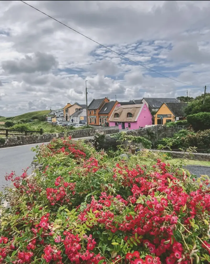 A colorful village street in Doolin with traditional thatched cottages and red flowers in the foreground.